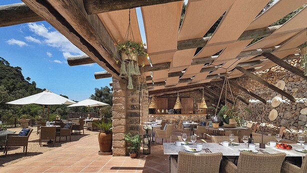 Une terrasse extérieure dotée d'un sol en pierre, de meubles en osier et de parasols pour créer de l'ombre.