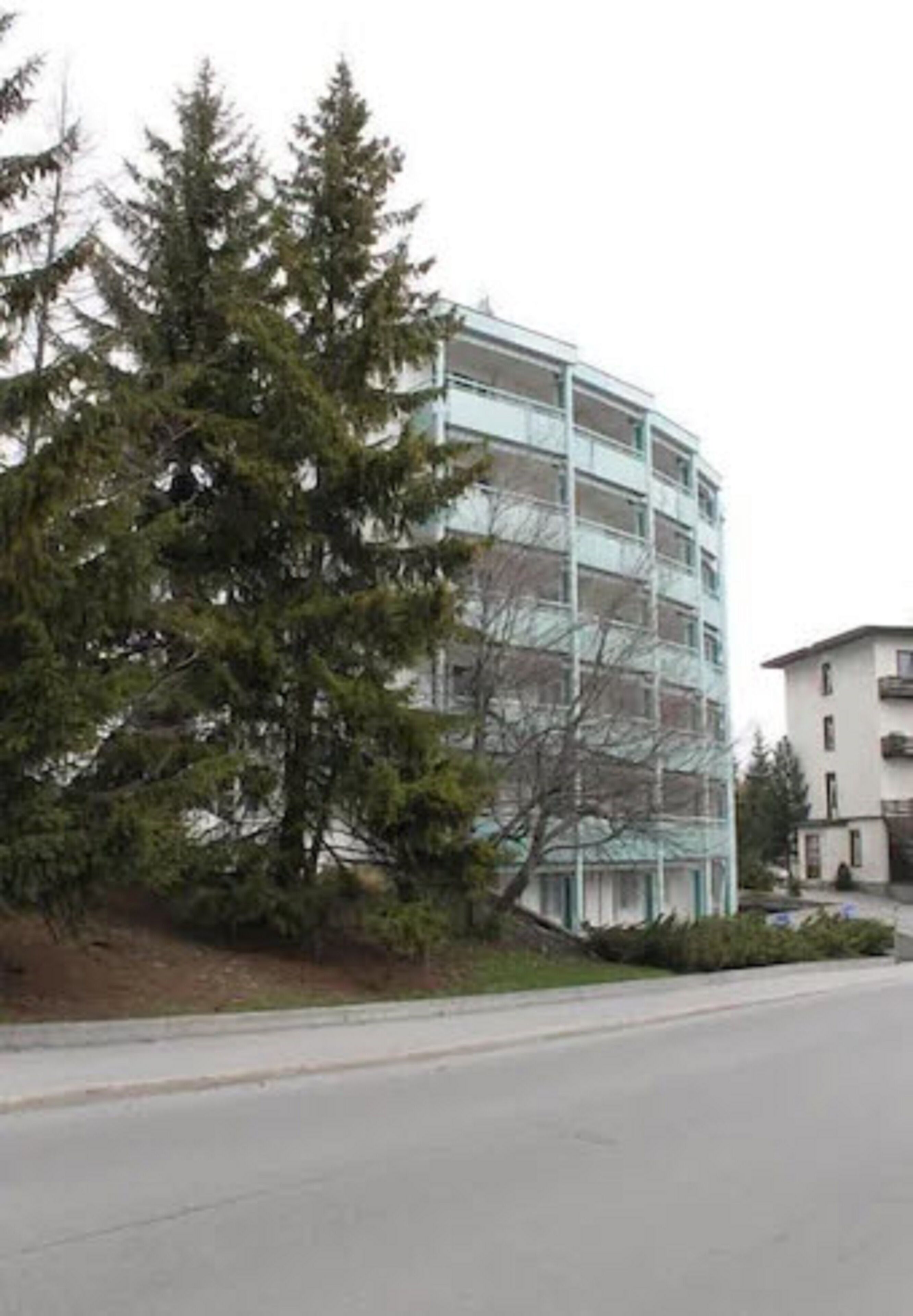 Un edificio de varios pisos con fachada de vidrio, rodeado de árboles.