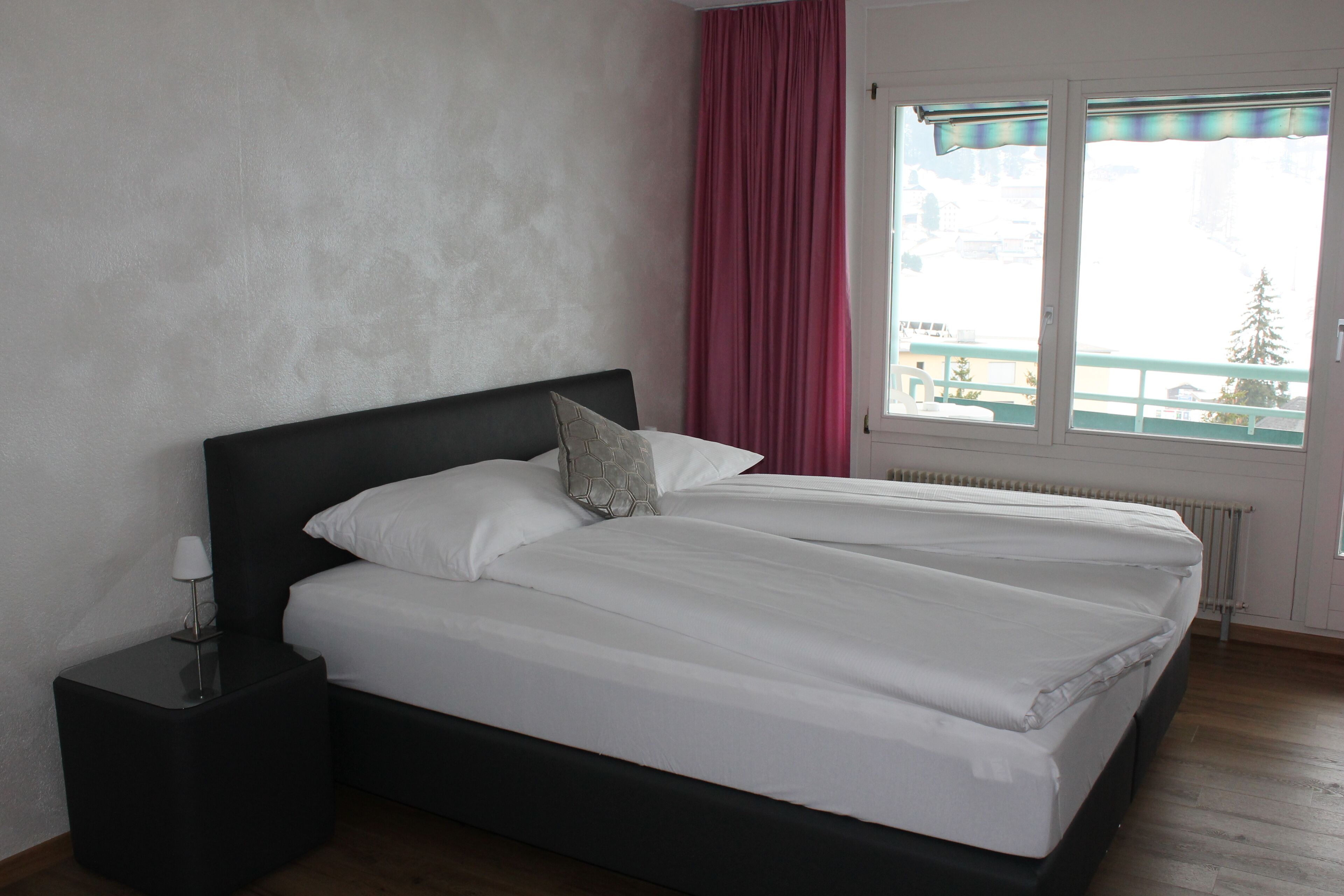 A double bed with white bedding, a black headboard, and a nightstand with a lamp.