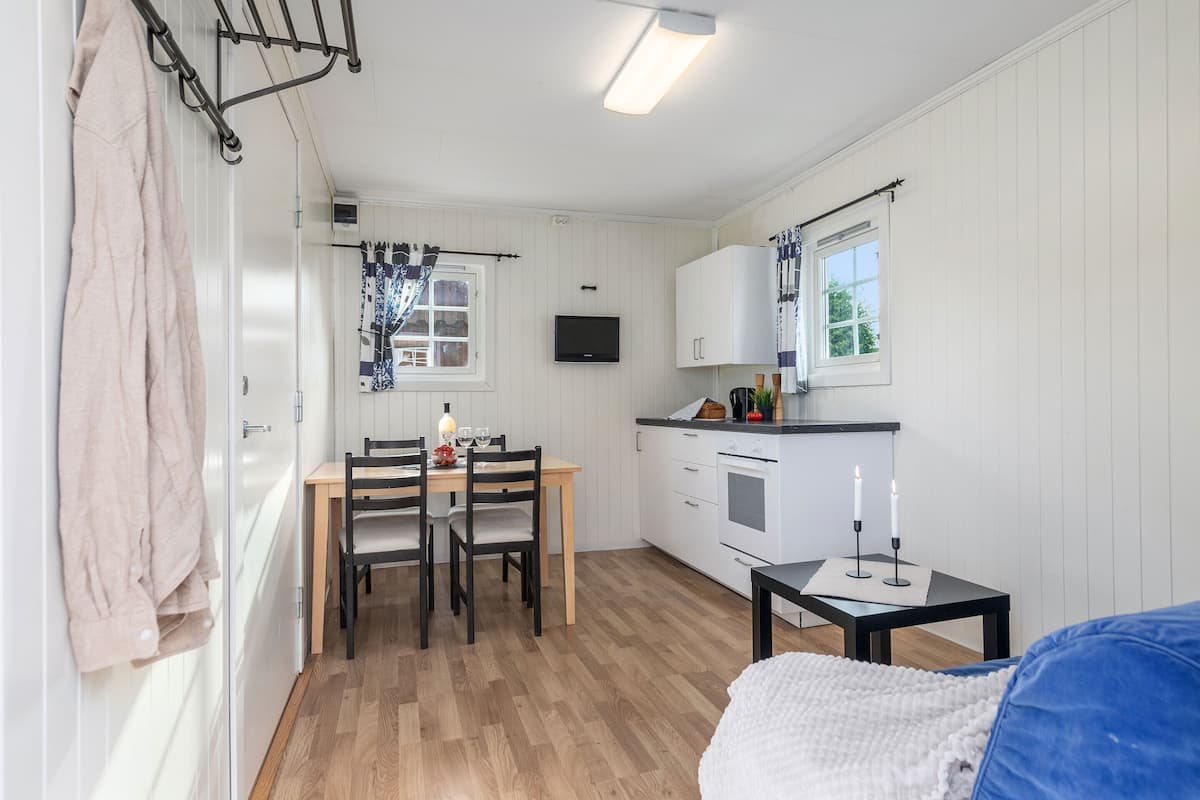 A compact kitchen with white cabinets, a dining table with chairs, a TV mounted above the counter, and a small table with candles.