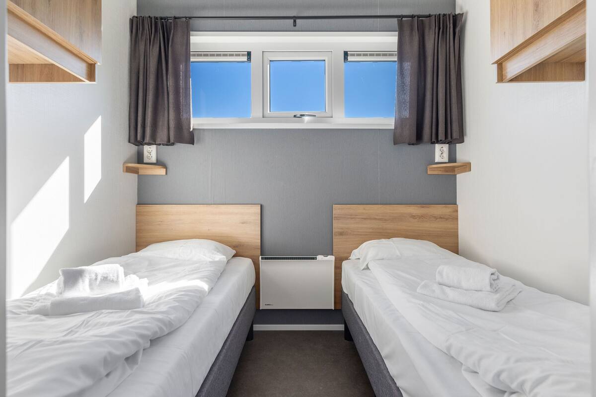 A compact bedroom with two single beds, a small window, and a built-in heater.