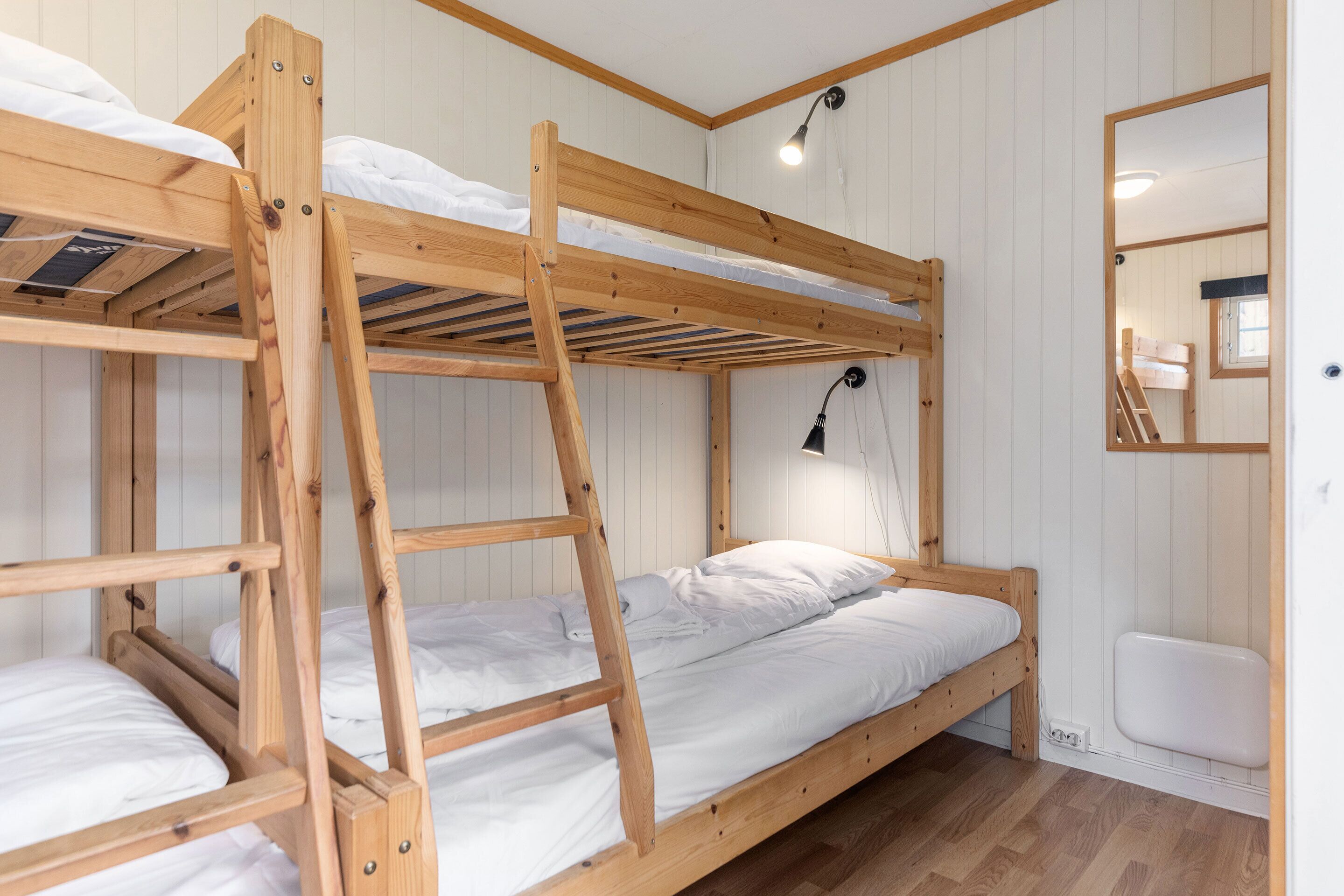 A bunk bed room with wooden frames, white bedding, and a small mirror on the wall.