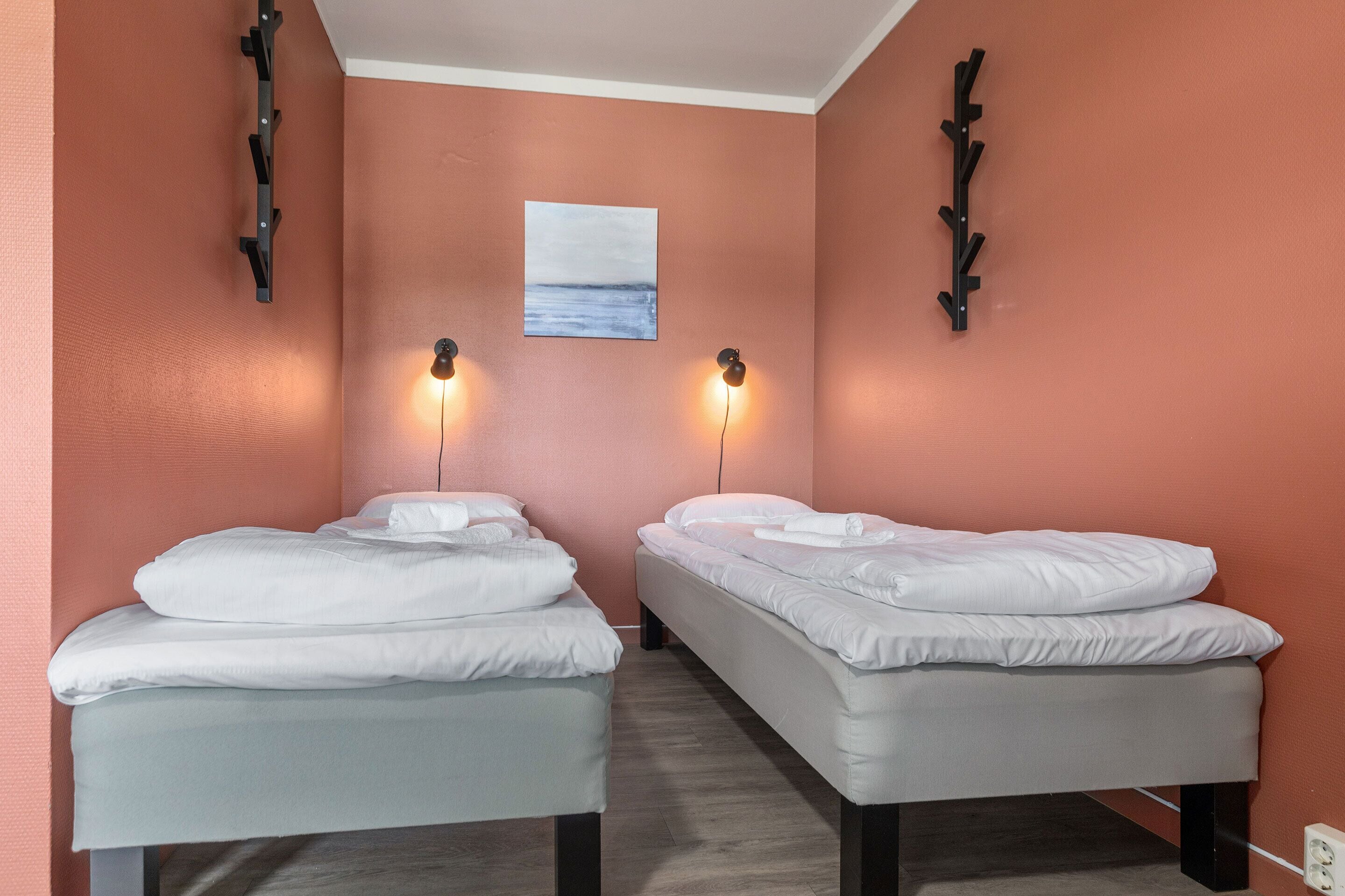 A room with two beds, a painting on the wall, and wall-mounted lights.