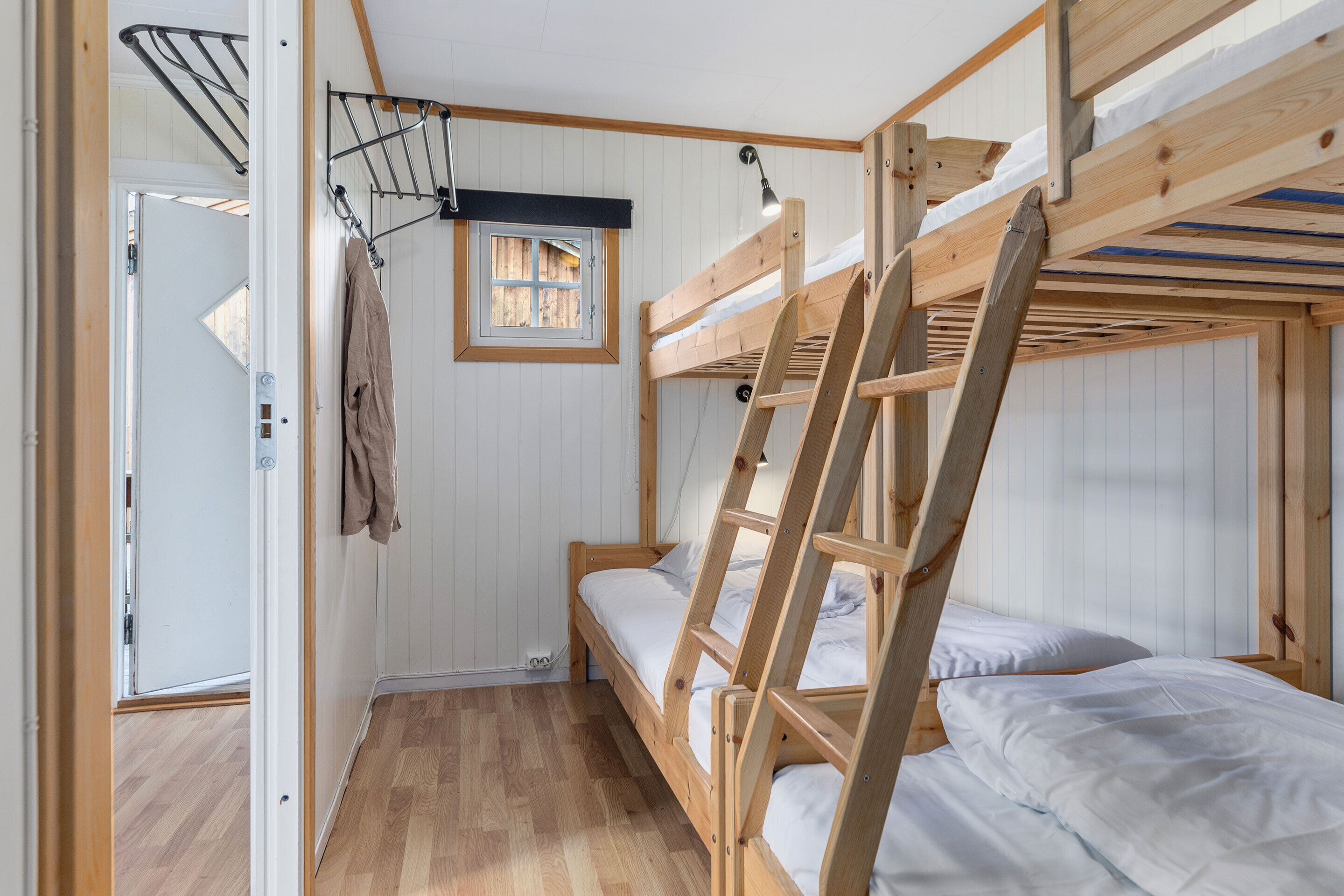 A compact room with a bunk bed, a small window, and a door leading to another room.