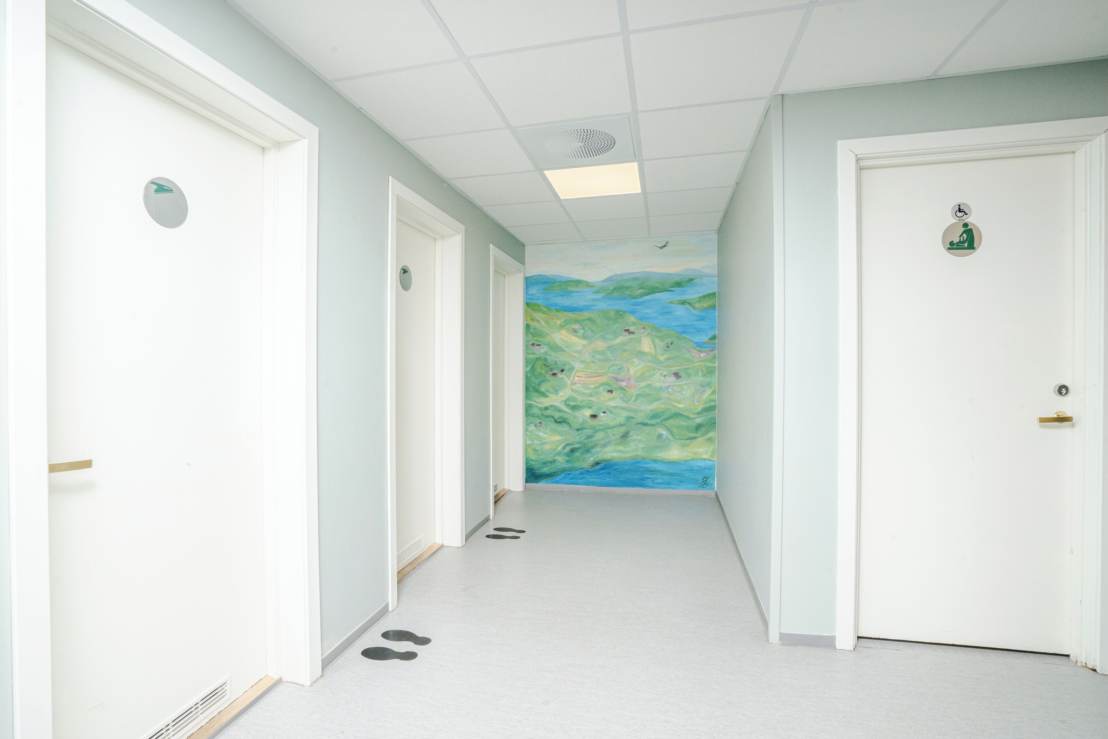 Un corridoio con pareti, porte e un murale raffigurante un paesaggio.