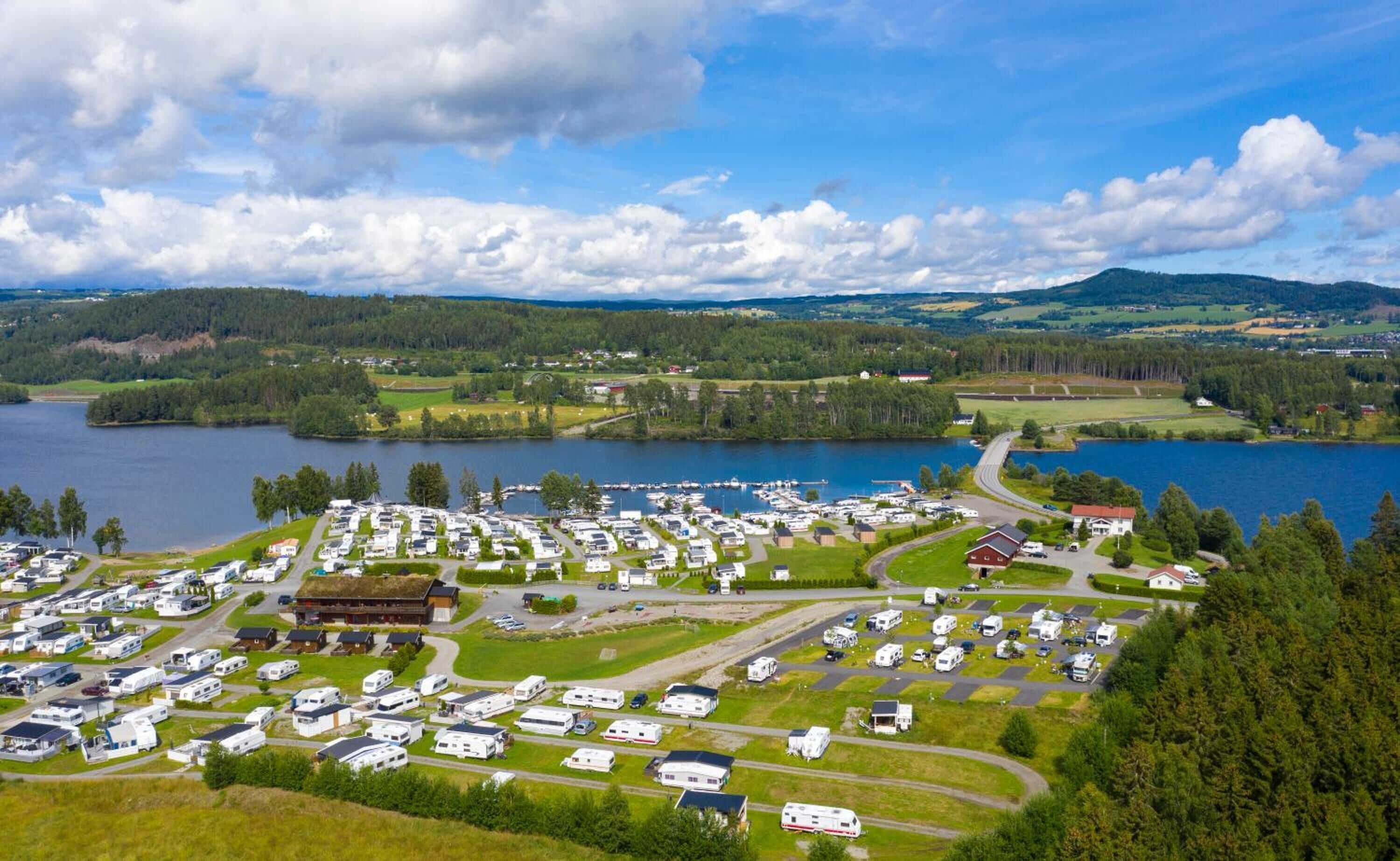 A campground with RVs and trailers, a large building, and a lake with boats.