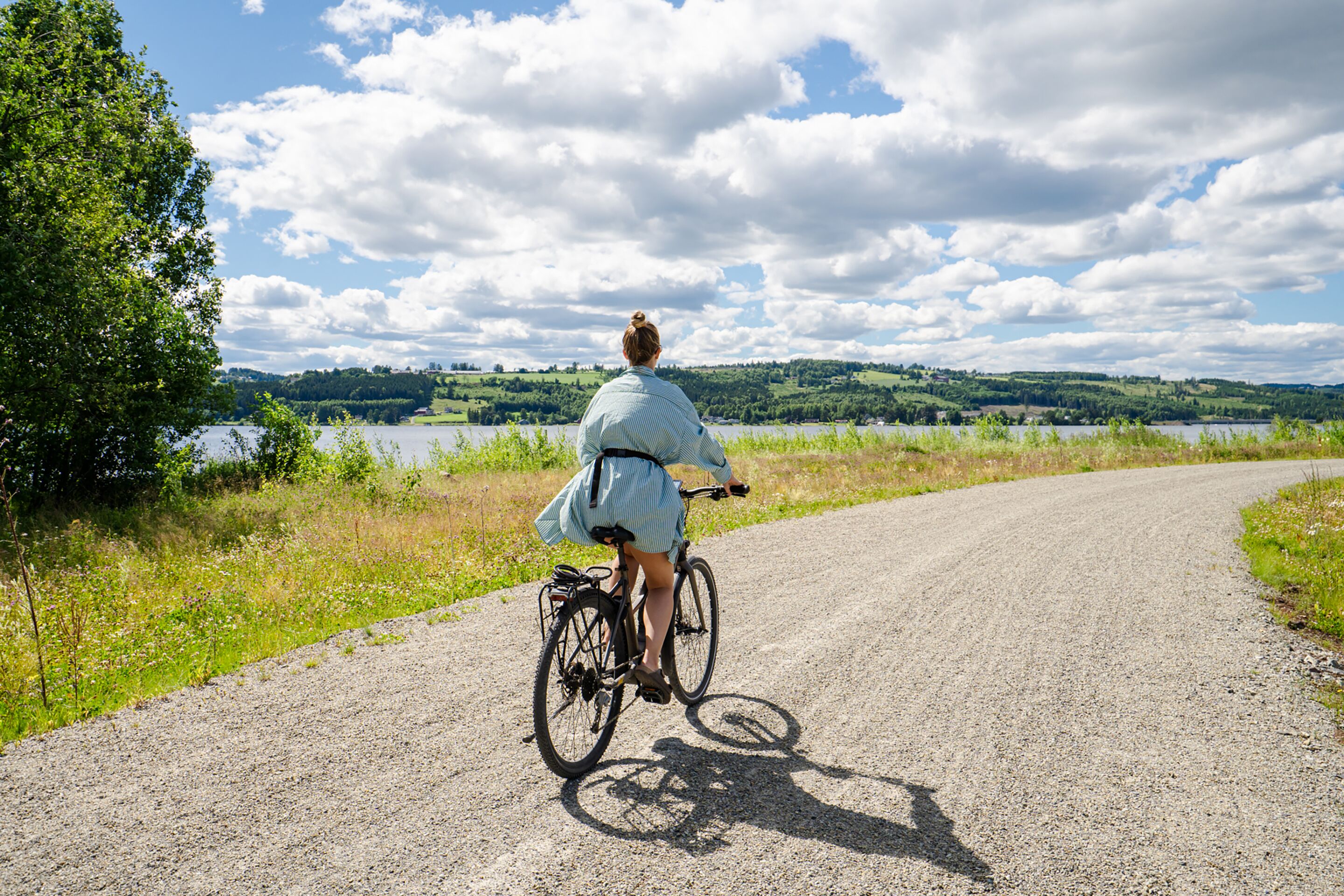 A person riding a bicycle on a gravel path with a lake and hills in the background.