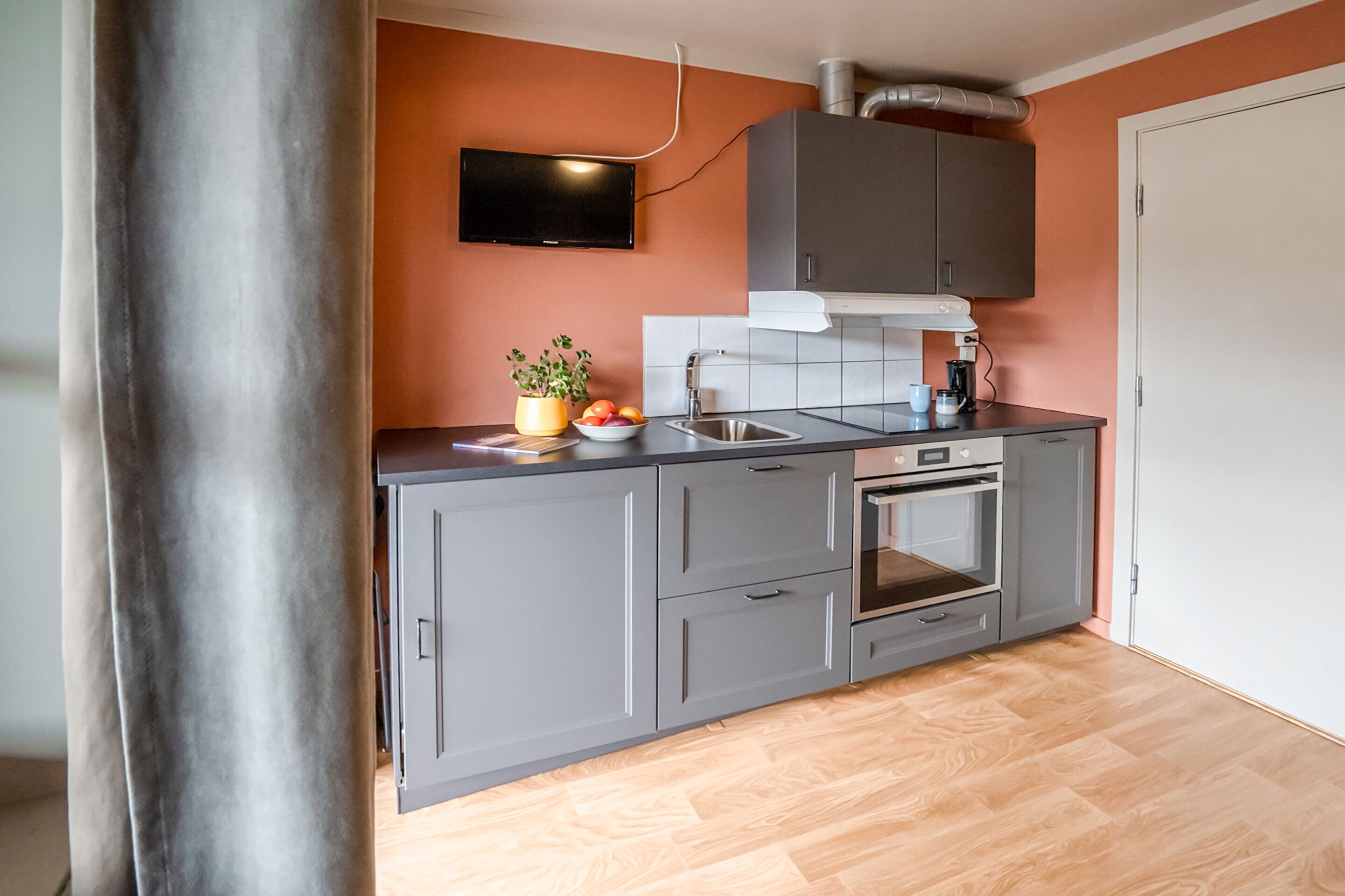 A modern kitchen with grey cabinets, a built-in oven, and a flat-screen TV mounted above the counter.