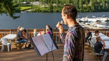 Una persona habla en un micrófono sobre una terraza de madera, con vistas a un lago y barcos al fondo.