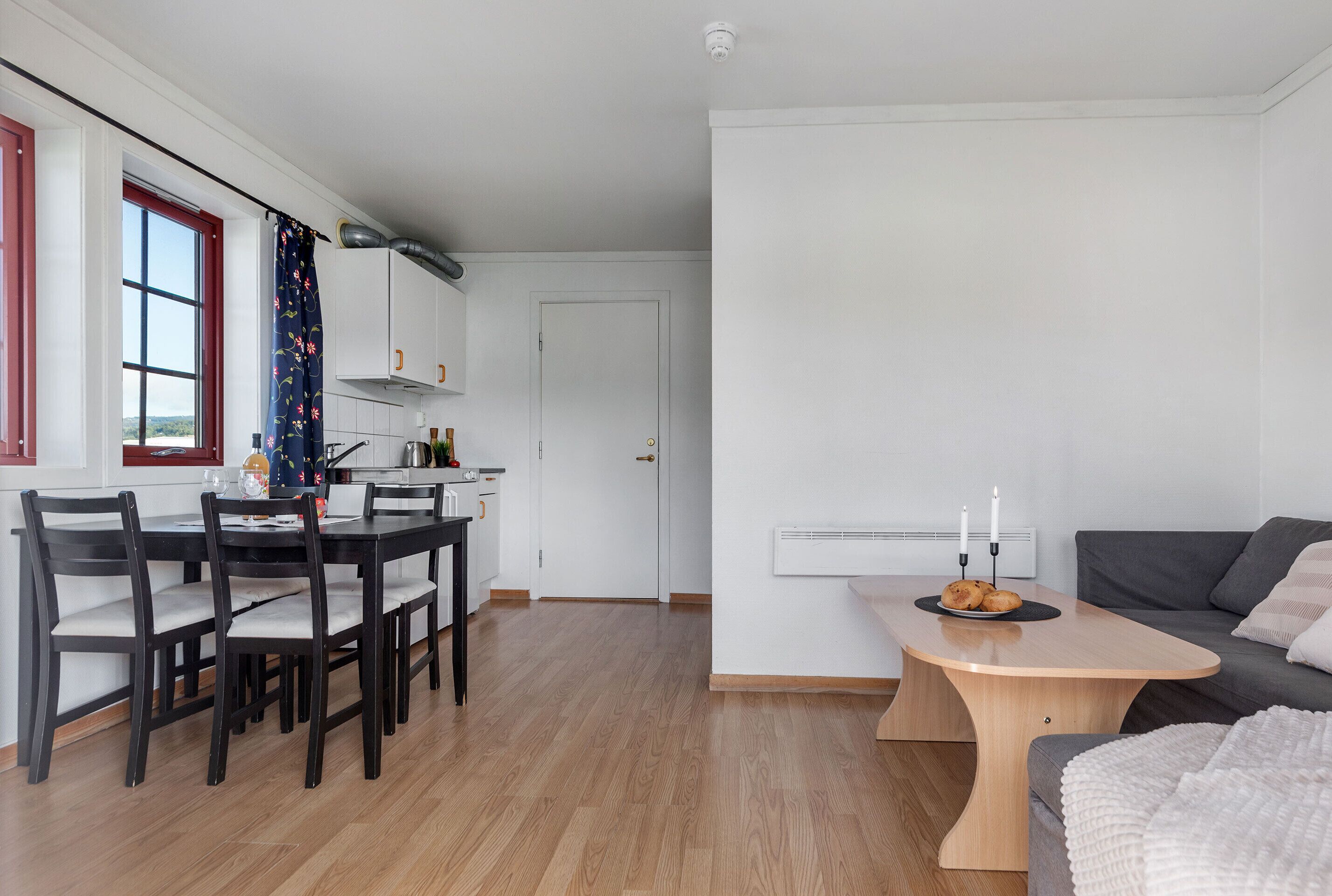 Ett modernt kök med vita skåp, ett matbord med stolar och en grå soffa i ett vardagsrum.