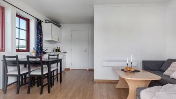 Ett modernt kök med vita skåp, ett matbord med stolar och en grå soffa i ett vardagsrum.