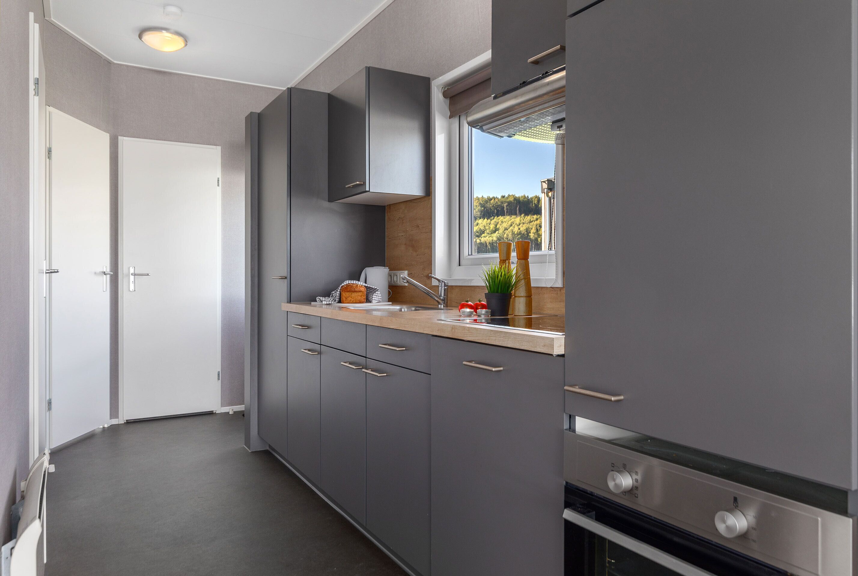 Een moderne keuken met grijze kastjes, een houten aanrechtblad en een raam met uitzicht op bomen.