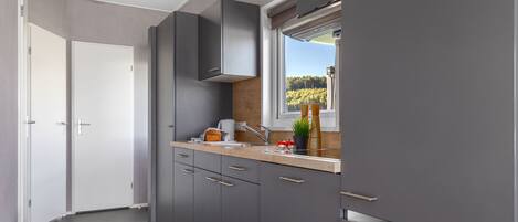 Een moderne keuken met grijze kastjes, een houten aanrechtblad en een raam met uitzicht op bomen.