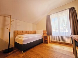 Un dormitorio con cama, mesita de noche, radiador y ventana con cortinas.