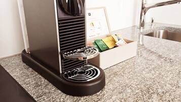 A kitchen with a coffee machine, a box of coffee pods, and a stainless steel sink.