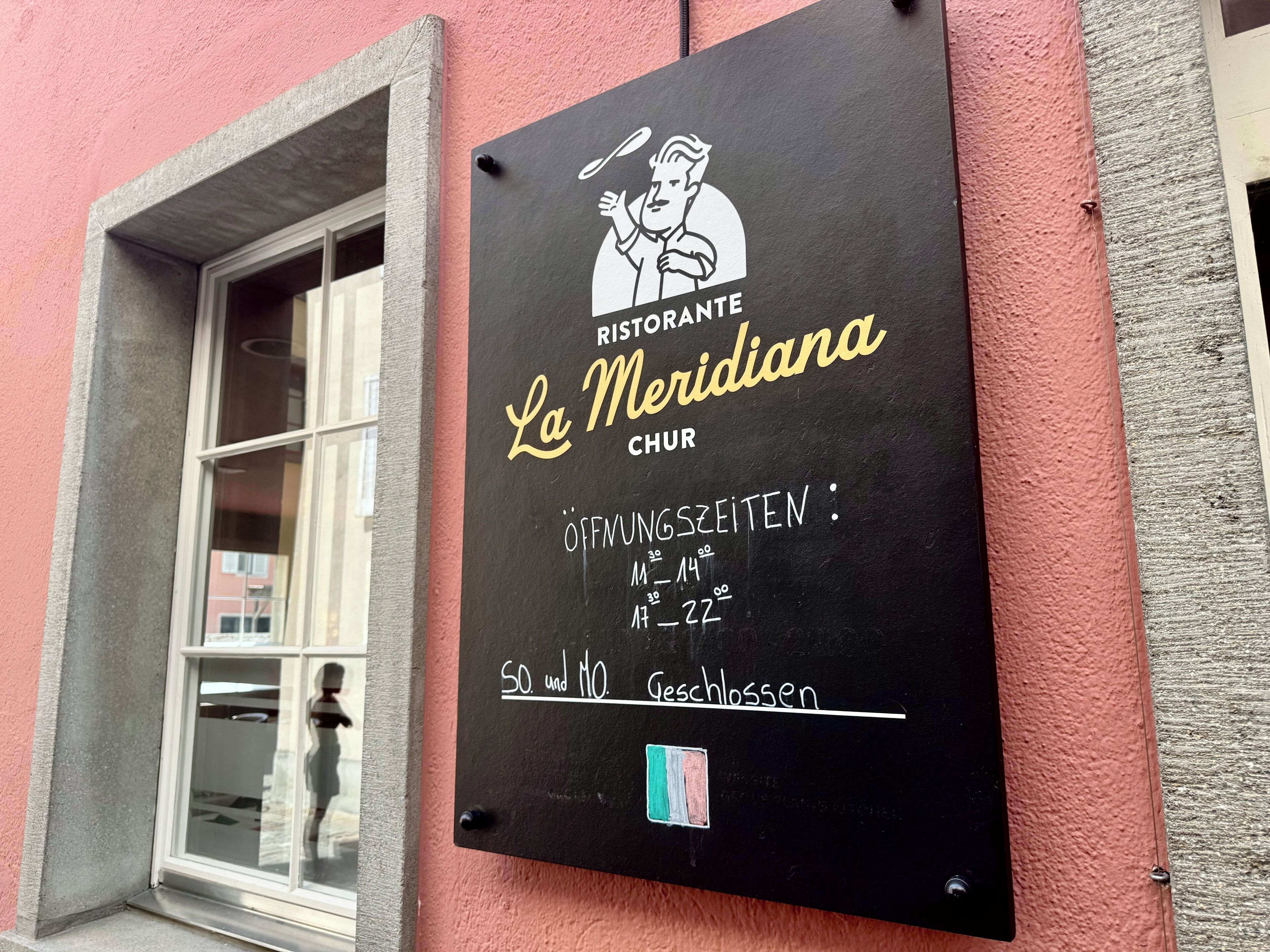 Un tableau noir indiquant les heures d’ouverture du restaurant et un autocollant représentant un drapeau.