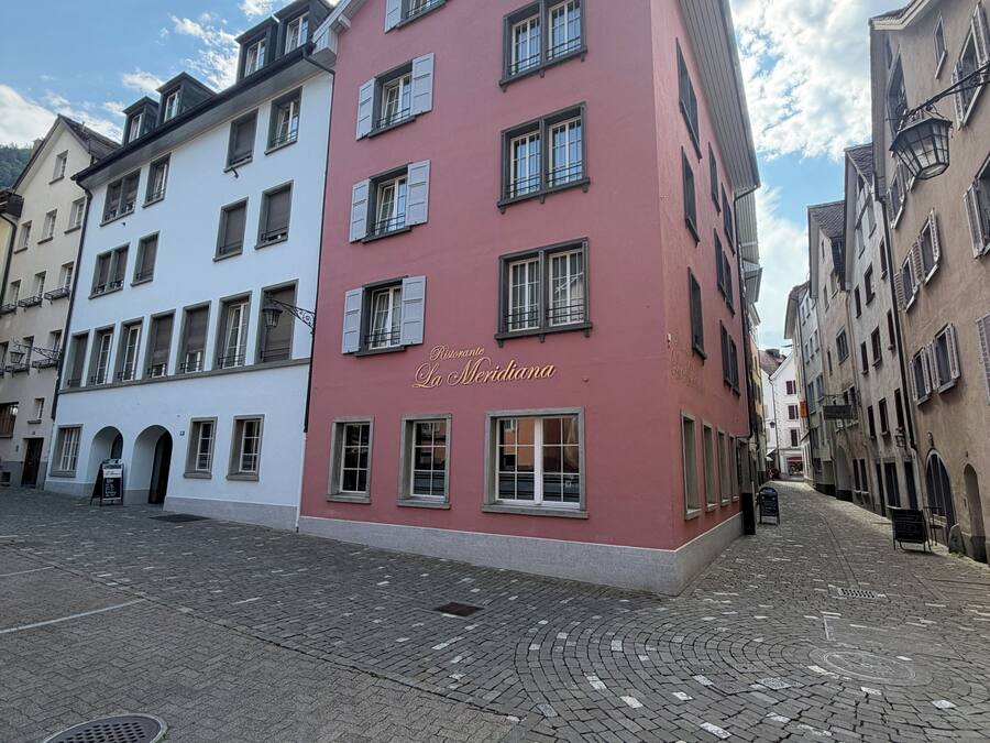A building with a red facade and multiple windows, a paved street in front, and other buildings around.