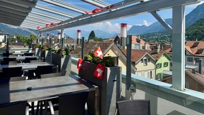 A terrace with outdoor seating, Swiss flags, and a mountain view. - Hotel Alpenstadt (Chur)