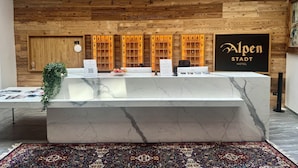 A hotel reception desk with a wooden wall backdrop, a framed sign, and a marble counter. - Hotel Alpenstadt (Chur)