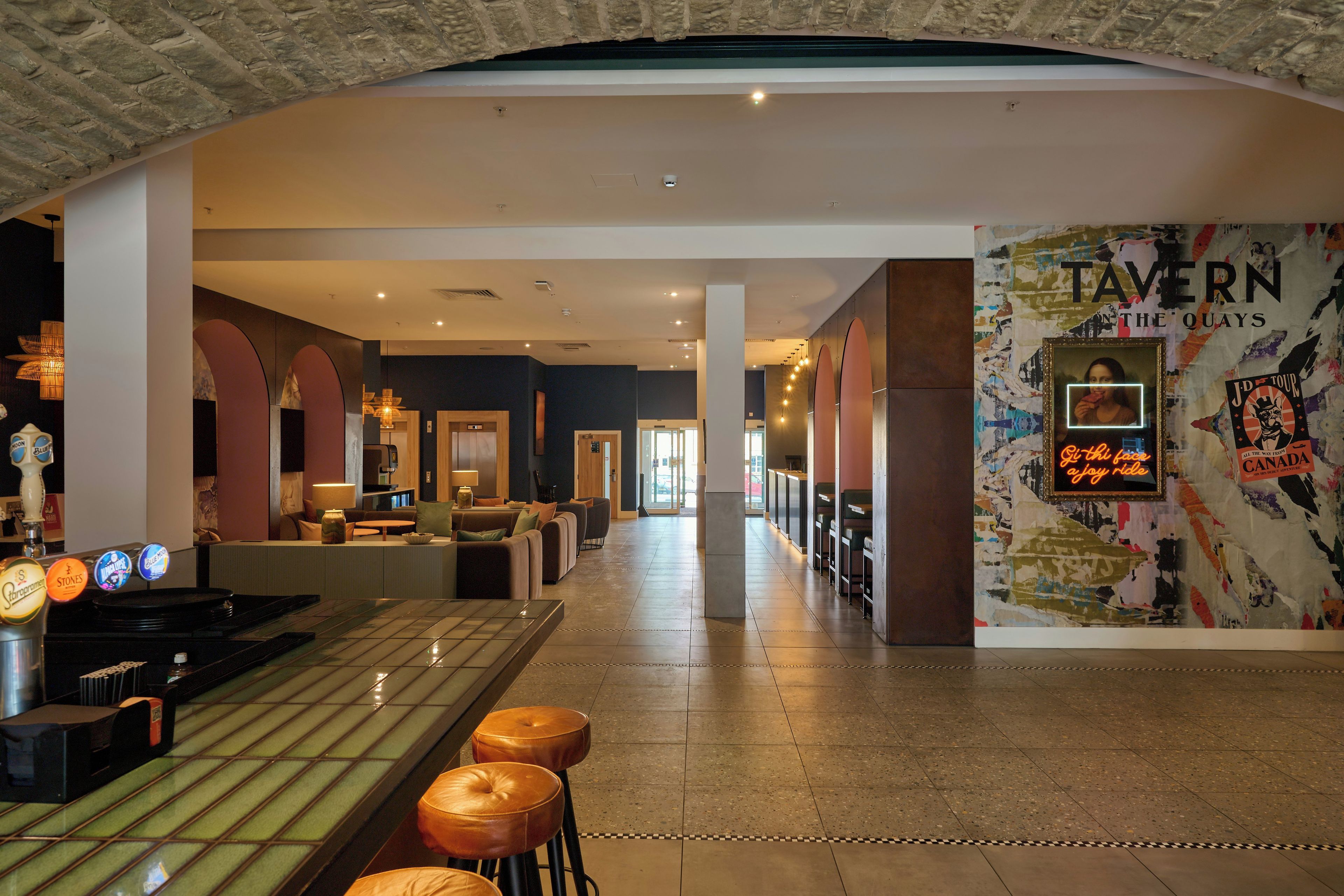 A modern bar area with a long counter, stools, and a wall with a poster.