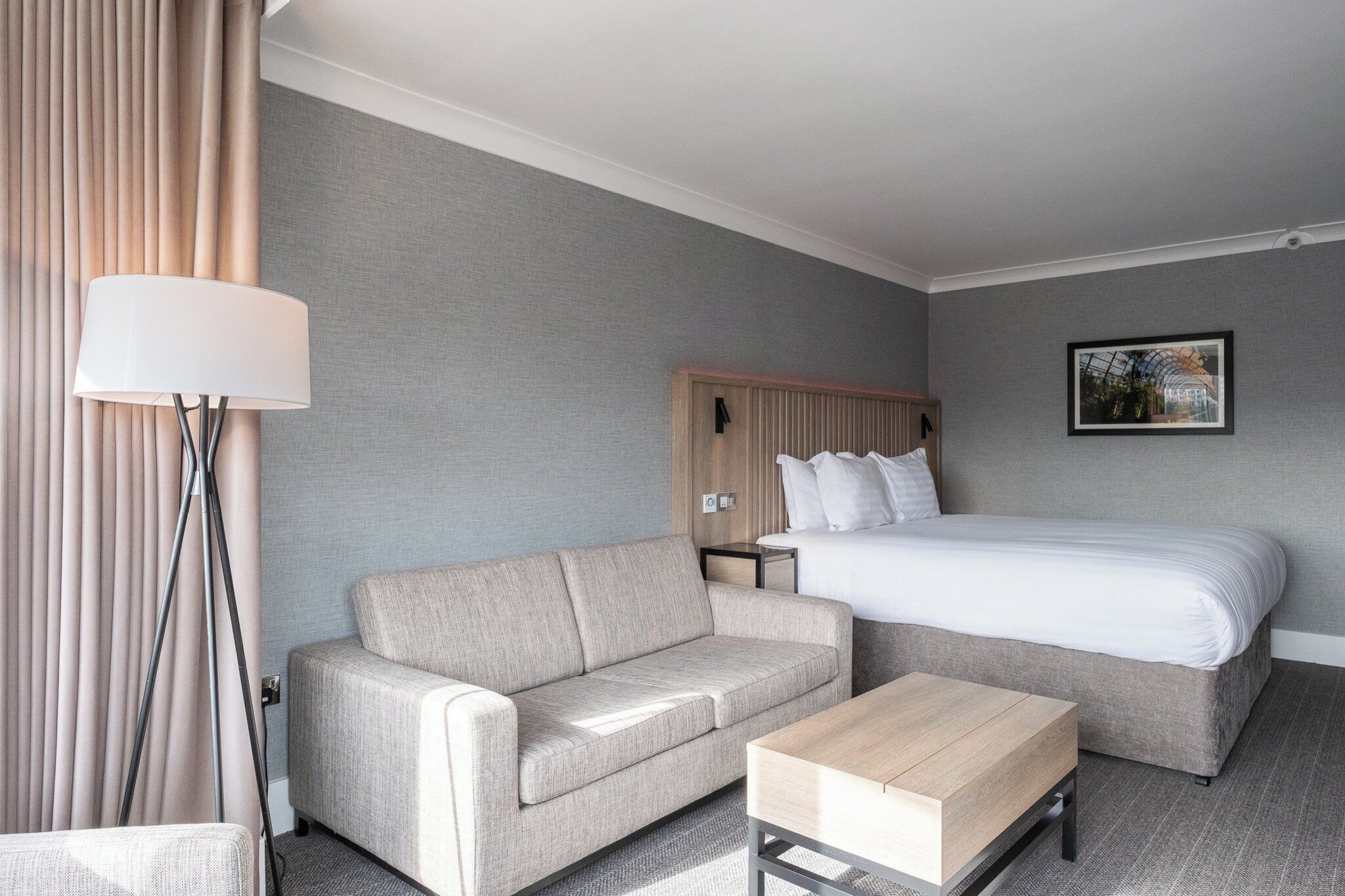 Hotellihuone, jossa on sänky, sohva, sohvapöytä, lamppu ja seinällä oleva kehystetty taulu.