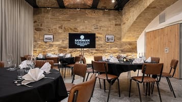 A conference room with multiple tables set for dining, stone walls, and a sign for Sandman Signature Sheffield Quays Hotel.