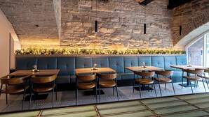 Een restaurant met stenen muren, houten tafels en blauwe zittingen met kussens.