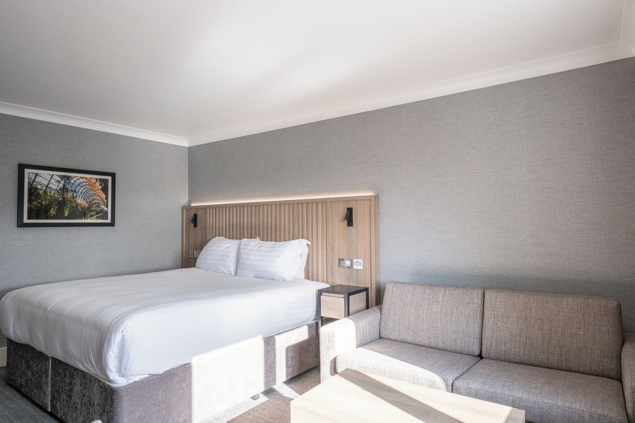 Una habitación de hotel moderna con una cama grande, un sofá y una mesita.