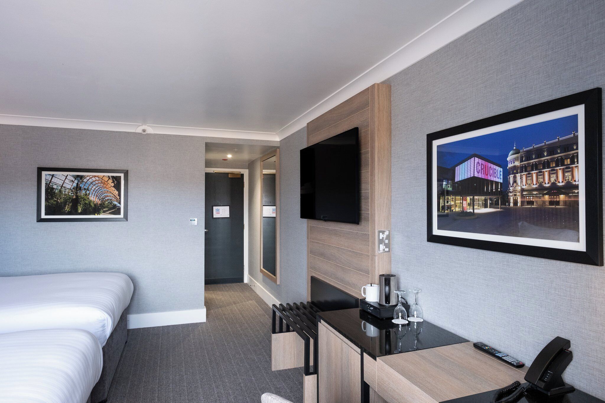 A hotel room with a bed, a desk with a coffee maker, a phone, and a TV mounted on the wall.