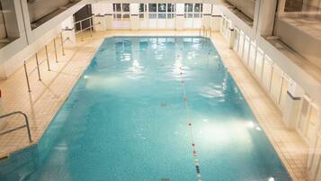 Ein Hallenbad mit klarem Wasser, gefliestem Boden und Metallgeländern.