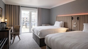 Een hotelkamer met twee bedden, een bureau, een stoel en uitzicht naar buiten.