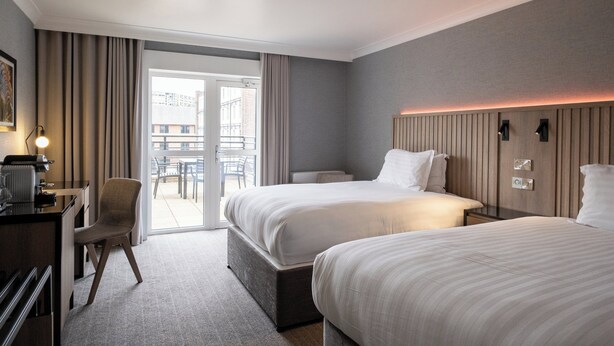 Habitación de hotel con dos camas, un escritorio, una silla y vistas al exterior.