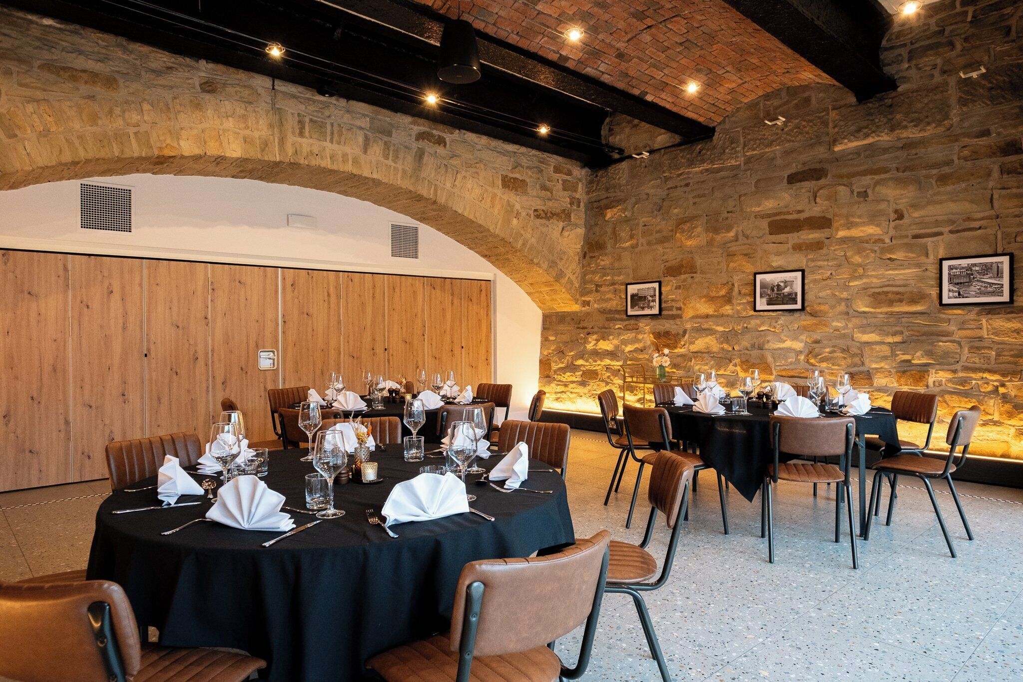 A dining area with round tables set for a meal, stone walls, and wooden paneling.