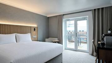 A hotel room with a large bed, a desk, a chair, and a view of the outdoors through a sliding door.