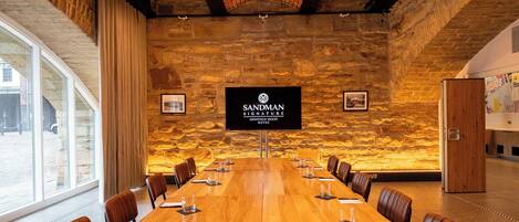 Un salón de conferencias con una larga mesa, sillas y una pantalla grande que muestra el nombre del hotel.