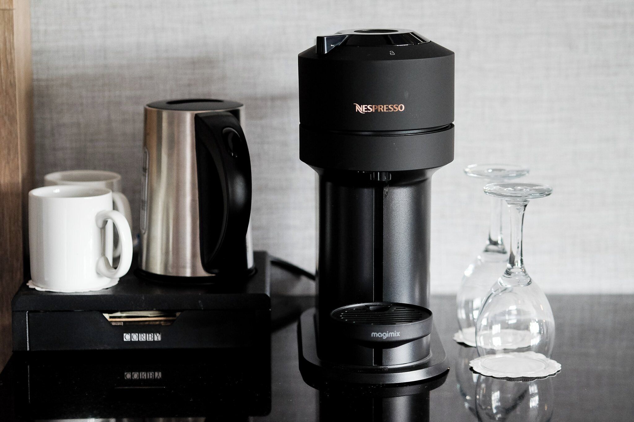 Une cafetière, une machine Nespresso et un verre à vin sont posés sur une table.