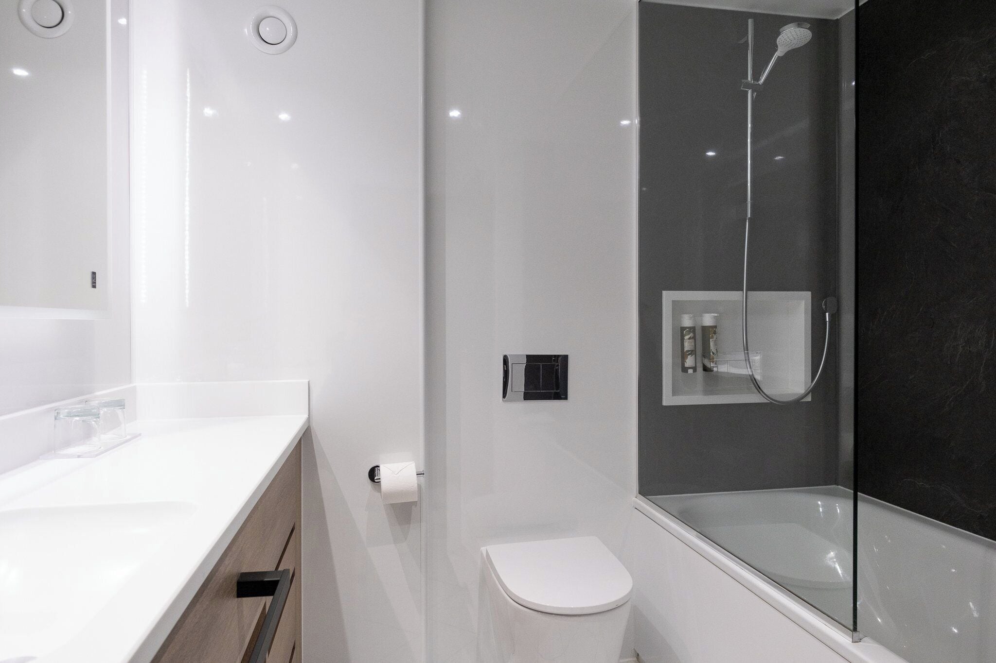 Une salle de bain moderne avec un meuble-lavabo blanc, des toilettes et une douche séparée par des parois en verre.
