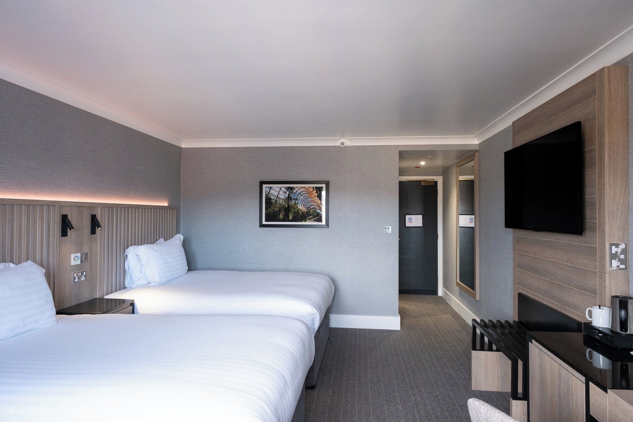 Een hotelkamer met twee bedden, een flatscreen televisie, een koffiezetapparaat en een ingelijste foto aan de muur.