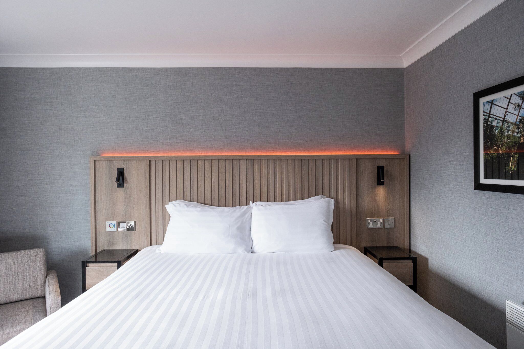 Una habitación de hotel moderna con una cama grande, dos mesitas de noche y un cabecero con iluminación integrada.