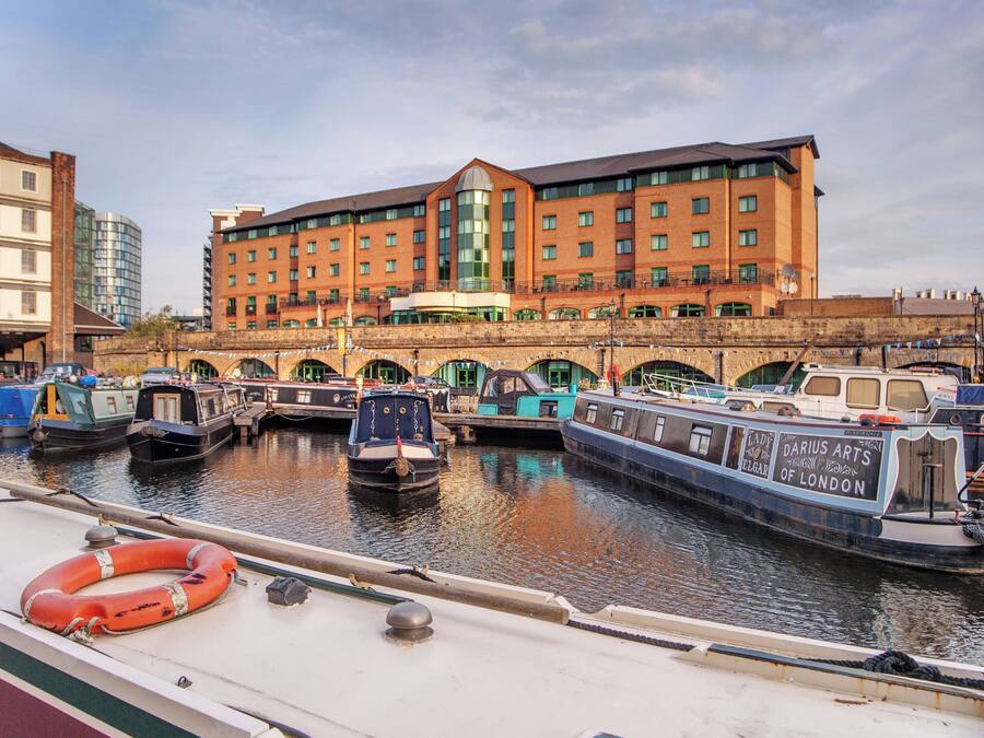 Un canal où sont amarrés des bateaux, un pont et un hôtel au design moderne.