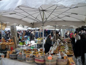 Ein lebhafter Markt im Freien mit verschiedenen Ständen, die Waren unter großen Sonnenschirmen anbieten.