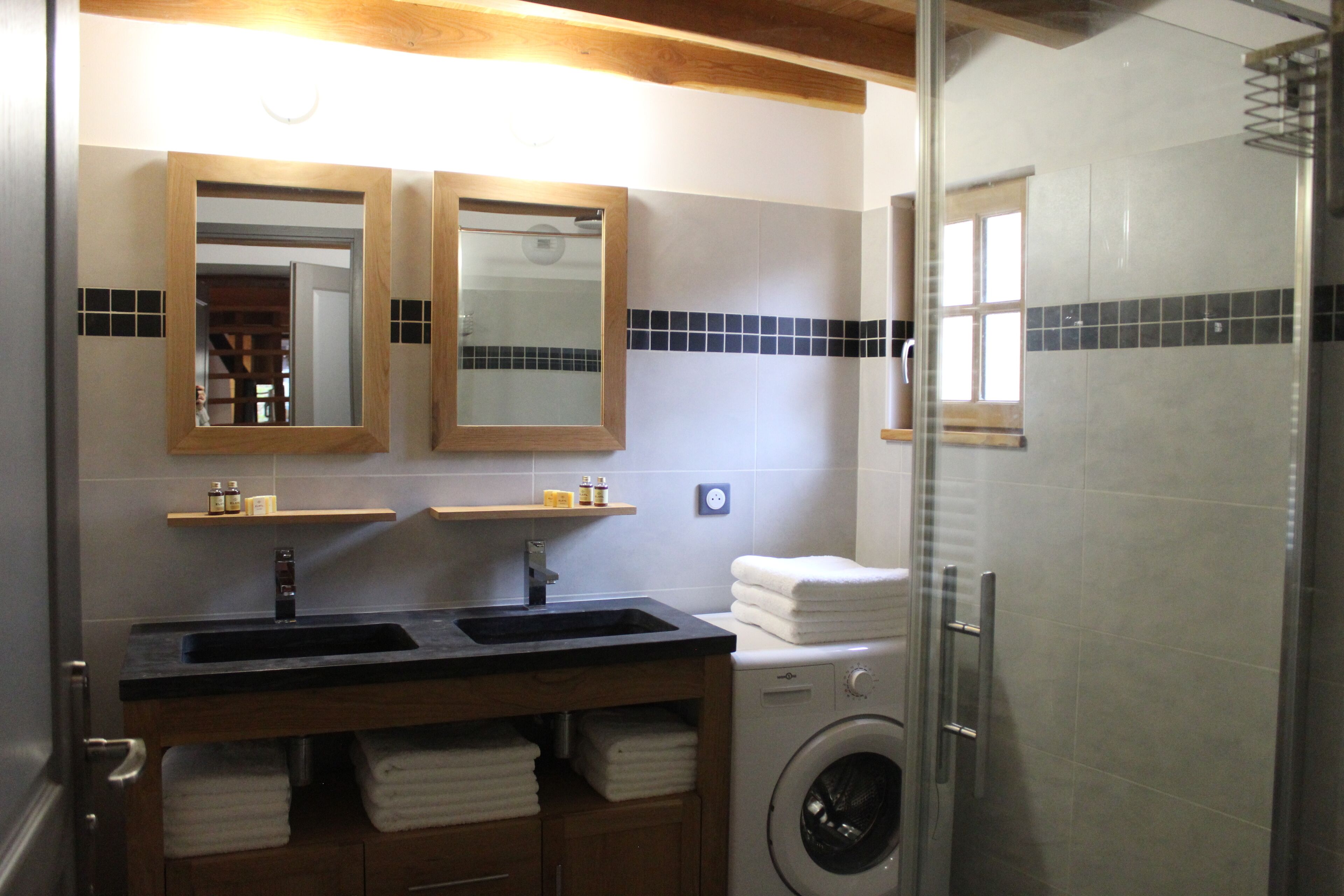 Ein Badezimmer mit einem Doppelwaschbecken, einem Holzbadezimmermöbel, einer Waschmaschine und einer Duschkabine aus Glas.