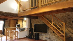 Ein rustikales Interieur mit einer Holztreppe, einer Küchenzeile inklusive Herd und einem an einer Steinwand befestigten Flachbildfernseher.