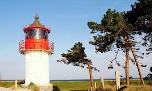 Un faro con parte superior roja, base blanca y cielo despejado al fondo.