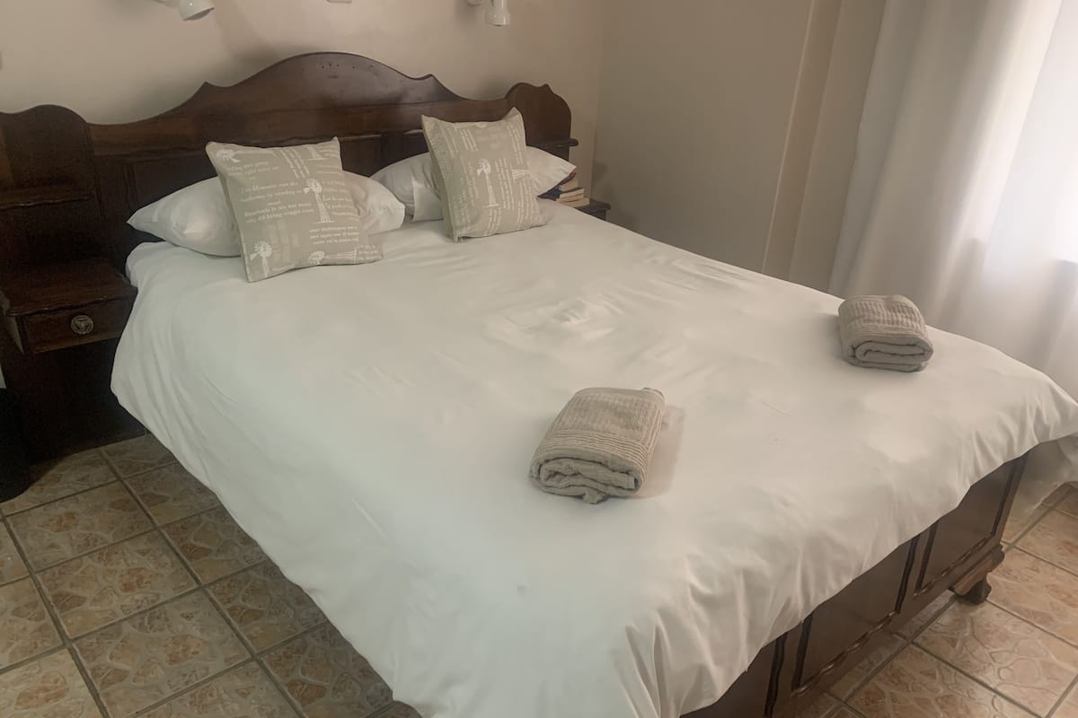 Una cama bien tendida con sábanas y almohadas blancas, un cabecero de madera y una toalla doblada en el piecero.