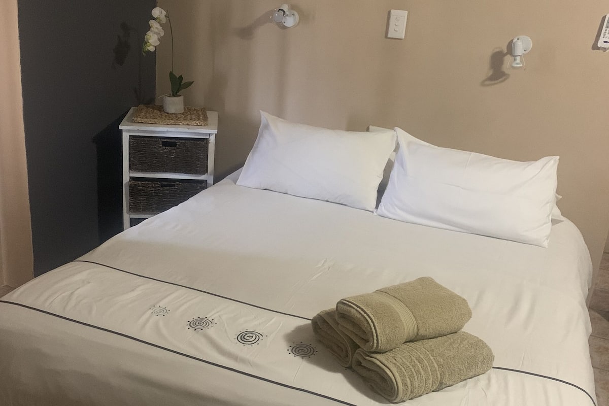 Una cama bien hecha con sábanas blancas y una toalla doblada al lado.