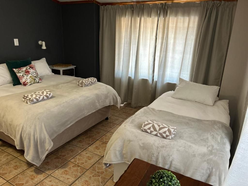 Een hotelkamer met twee bedden, een tafeltje en een raam met gordijnen.