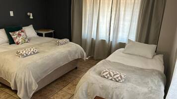 Een hotelkamer met twee bedden, een tafeltje en een raam met gordijnen.