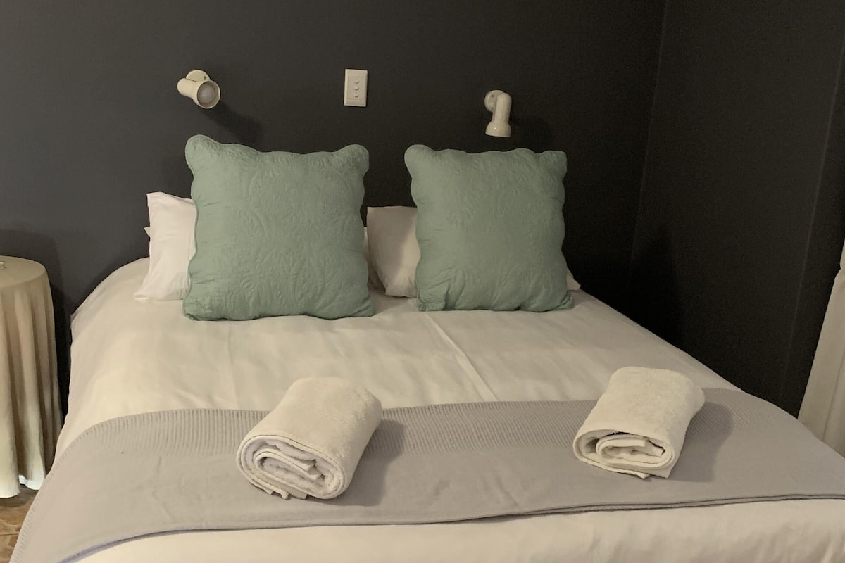 Una cama bien hecha con dos almohadas, una toalla doblada y una manta.