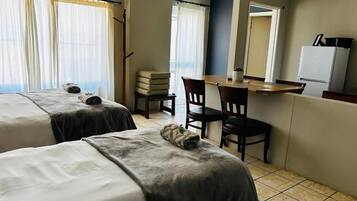 Une chambre d’hôtel avec deux lits, un bureau avec des chaises, un réfrigérateur et une fenêtre avec des rideaux.
